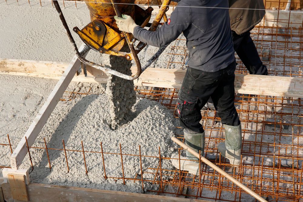 Cumuli ordinati di pietrisco e inerti da costruzione in un piazzale industriale, con mezzi di cantiere sullo sfondo.