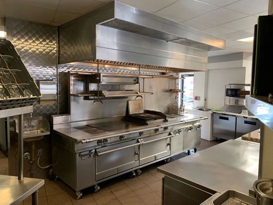 A commercial kitchen with stainless steel appliances, including a stove, vent hood, and refrigerators.