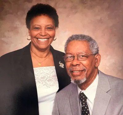 Smiling couple posed against a soft beige studio backdrop, wearing formal attire.