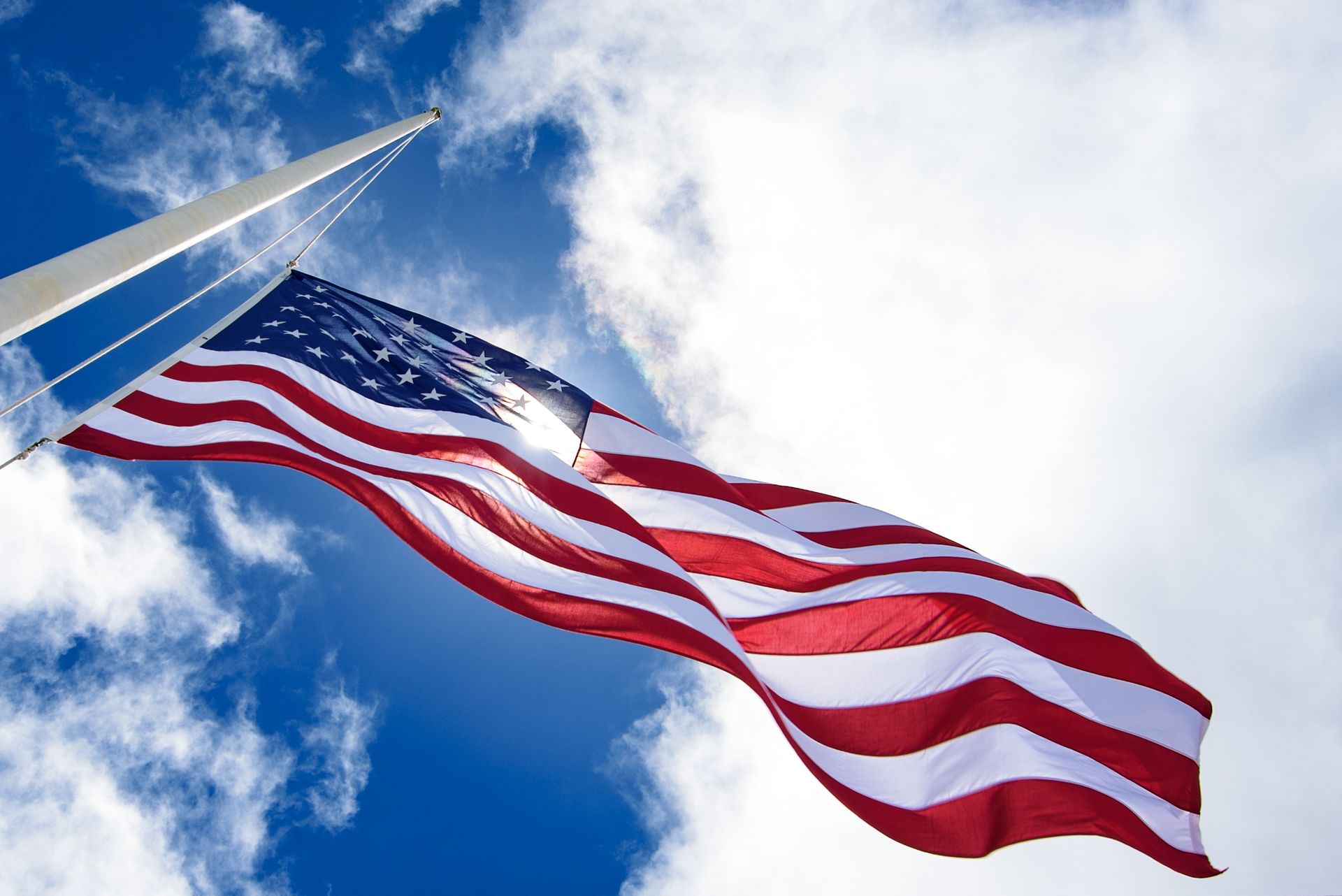 American flag waving on a flagpole against a partly cloudy blue sky.