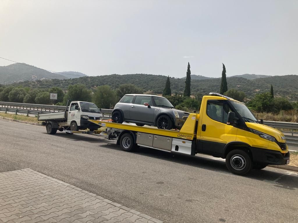 Yellow tow truck carrying a gray SUV on a roadside with hills in the background