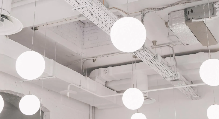 White, spherical pendant lights illuminate a white ceiling with exposed pipes. Sky-Walker White, spherical pendant lights illuminate a white ceiling with exposed pipes. Sky-Walker