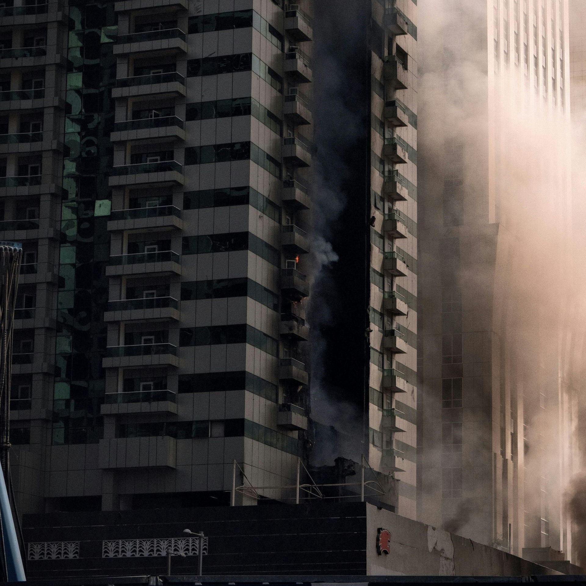 Tall apartment buildings shrouded in dust and smoke, with a dark street-level barrier in front Tall apartment buildings shrouded in dust and smoke, with a dark street-level barrier in front