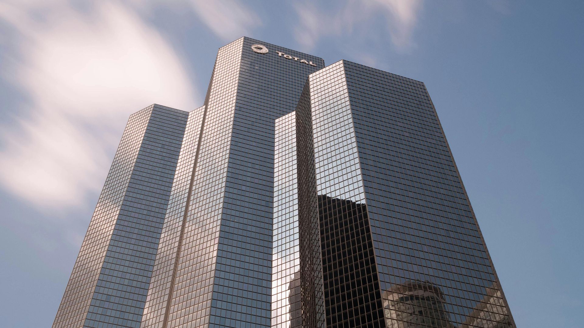 The TotalEnergies skyscraper in La Défense, Paris, seen from a low angle against a cloudy blue sky.