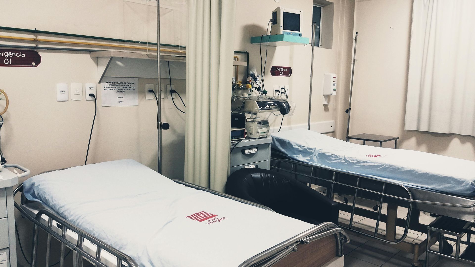 Two hospital beds with light blue sheets and medical equipment in a shared patient room.