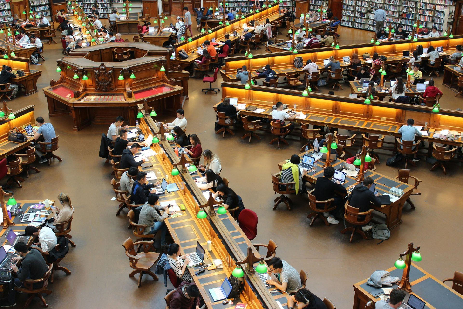 High-angle view of a library filled with people studying at long, illuminated wooden tables.