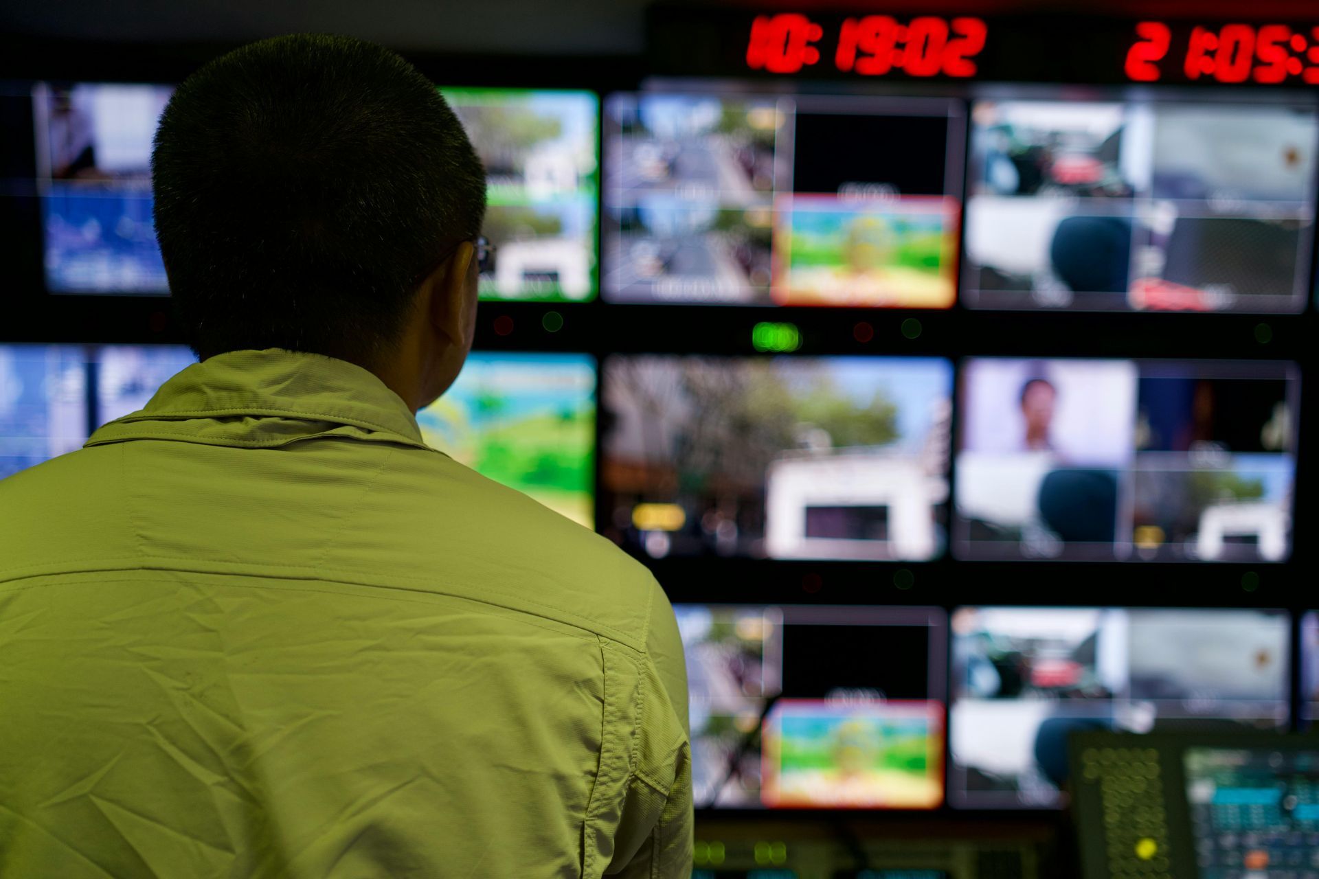 Person in a yellow shirt facing a wall of security monitors controled by Sky-Walker in a control room. Person in a yellow shirt facing a wall of security monitors controled by Sky-Walker in a control room.