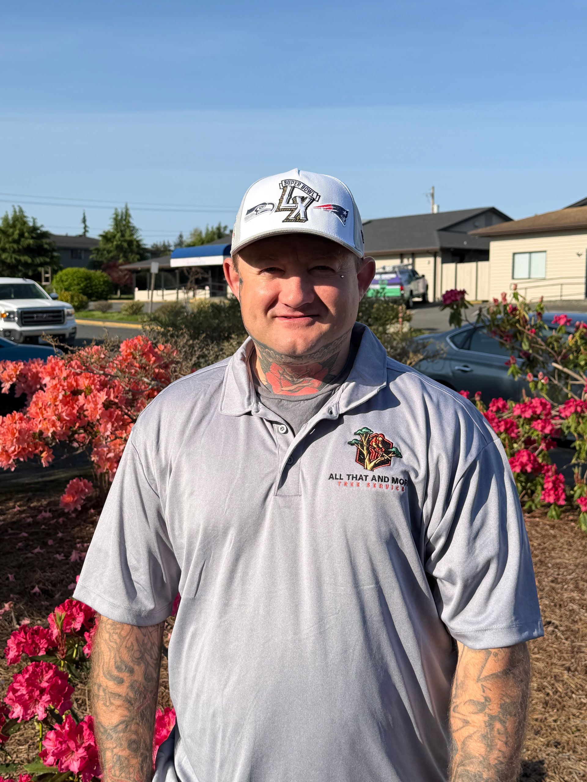 Man standing in a gray polo and white cap beside colorful flower beds on a sunny day