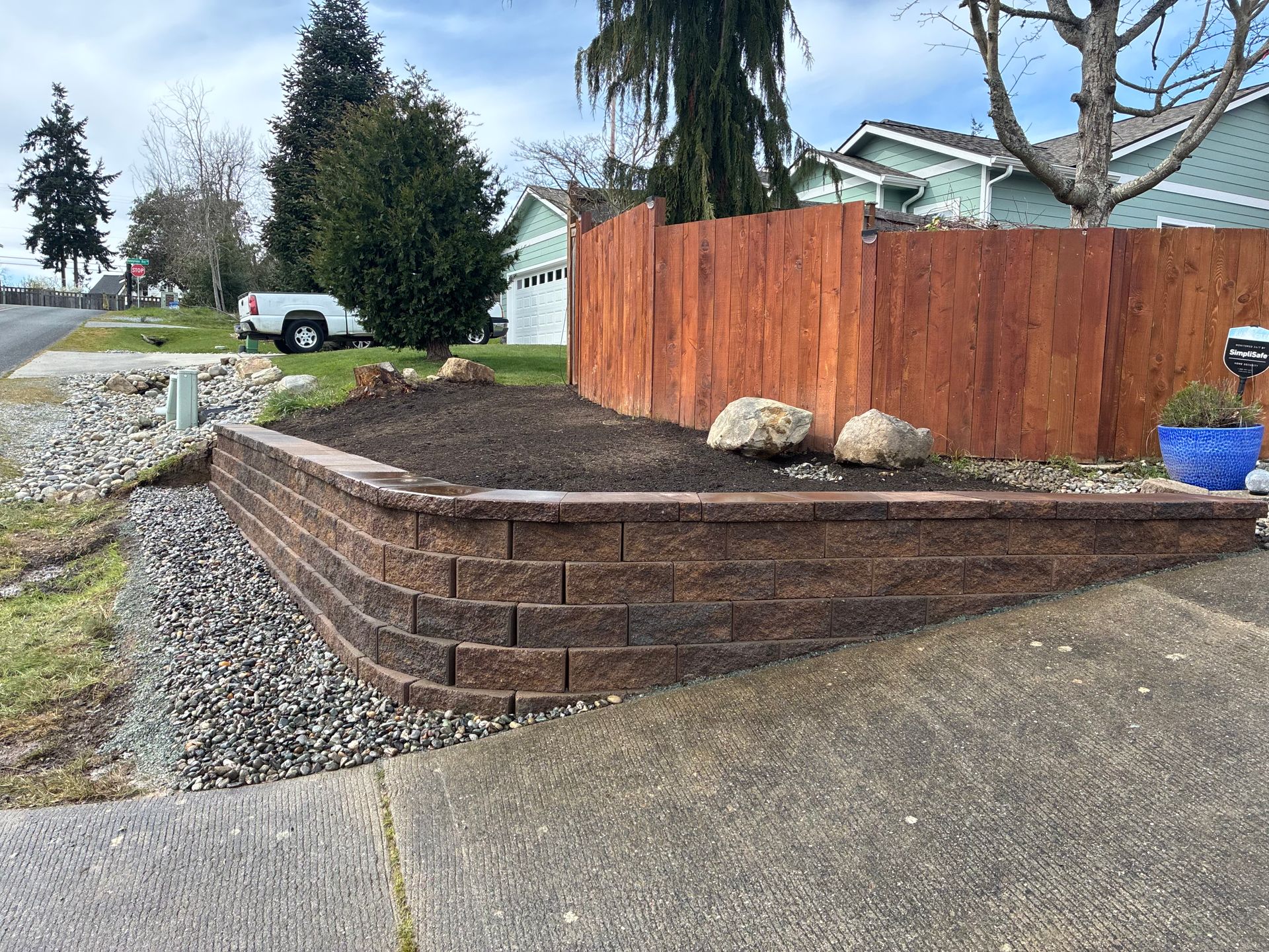 Tiered brick retaining wall with gravel slope and landscaped dirt bed beside a driveway in a suburban yard