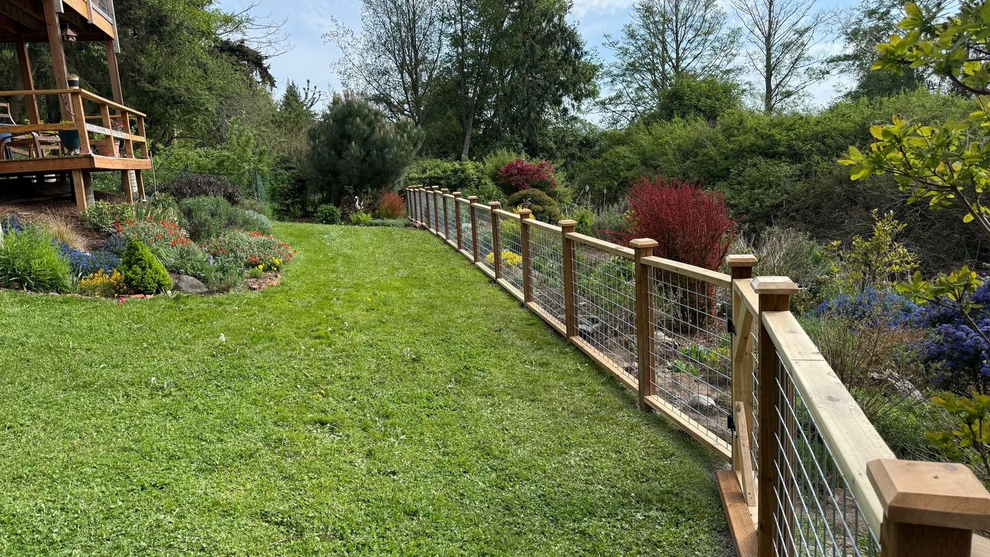 Wooden-railed garden walkway beside a green lawn and colorful flower beds under a sunny sky