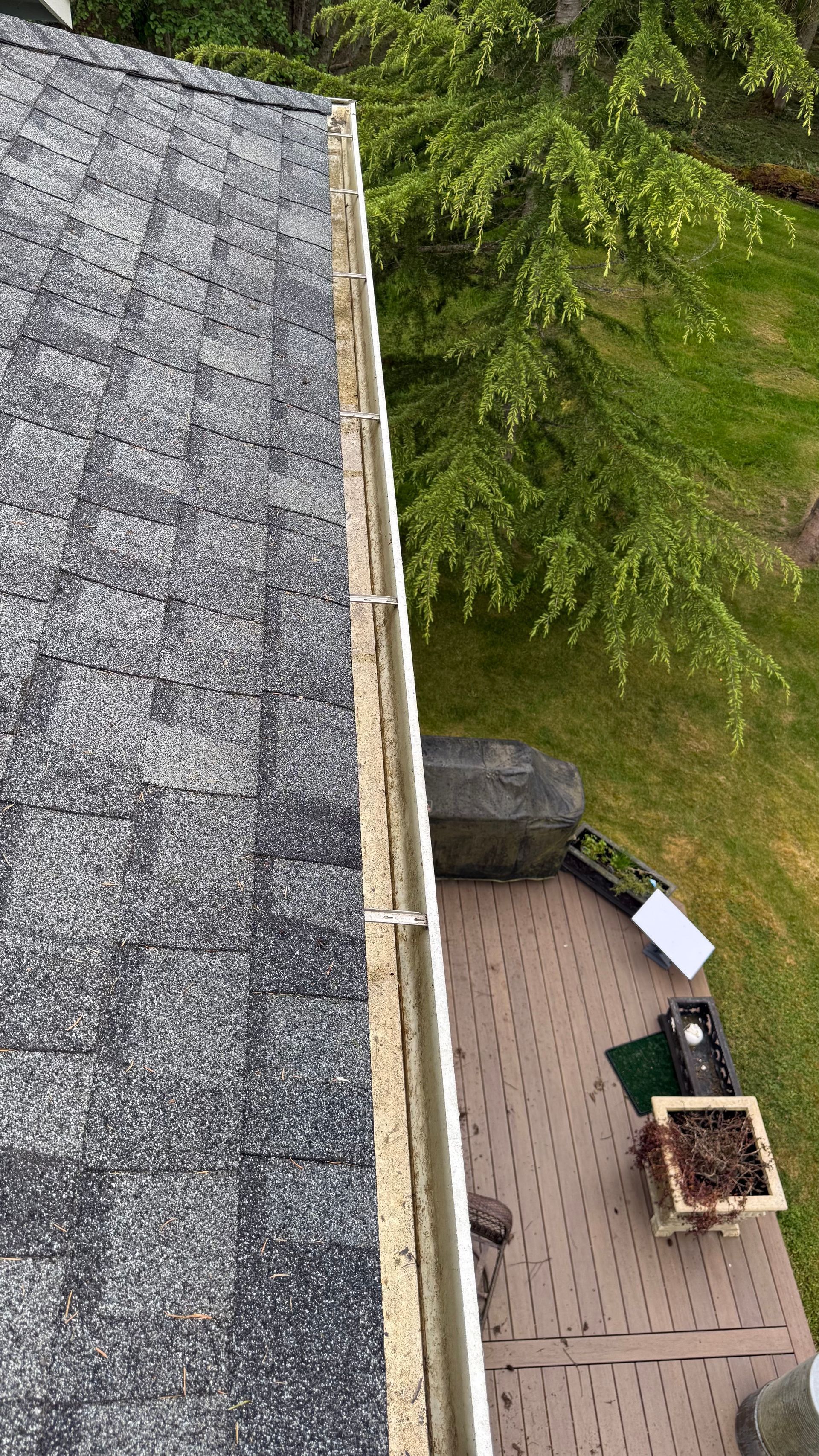 Aerial view of a roof, deck, and grassy yard with outdoor furniture and a grill.