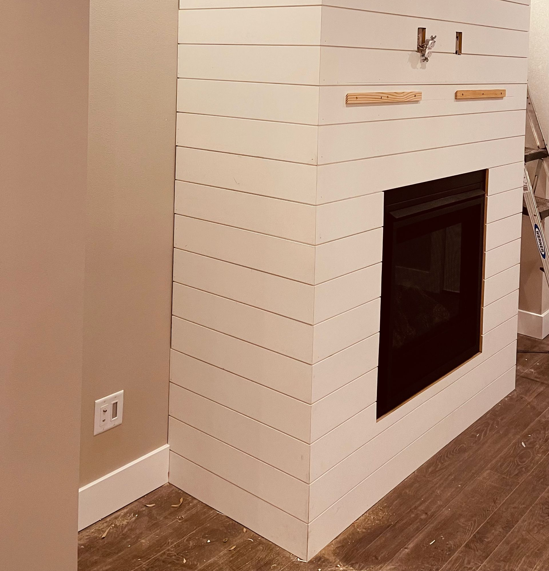 White shiplap fireplace wall with black insert in a room with wood floor and beige walls