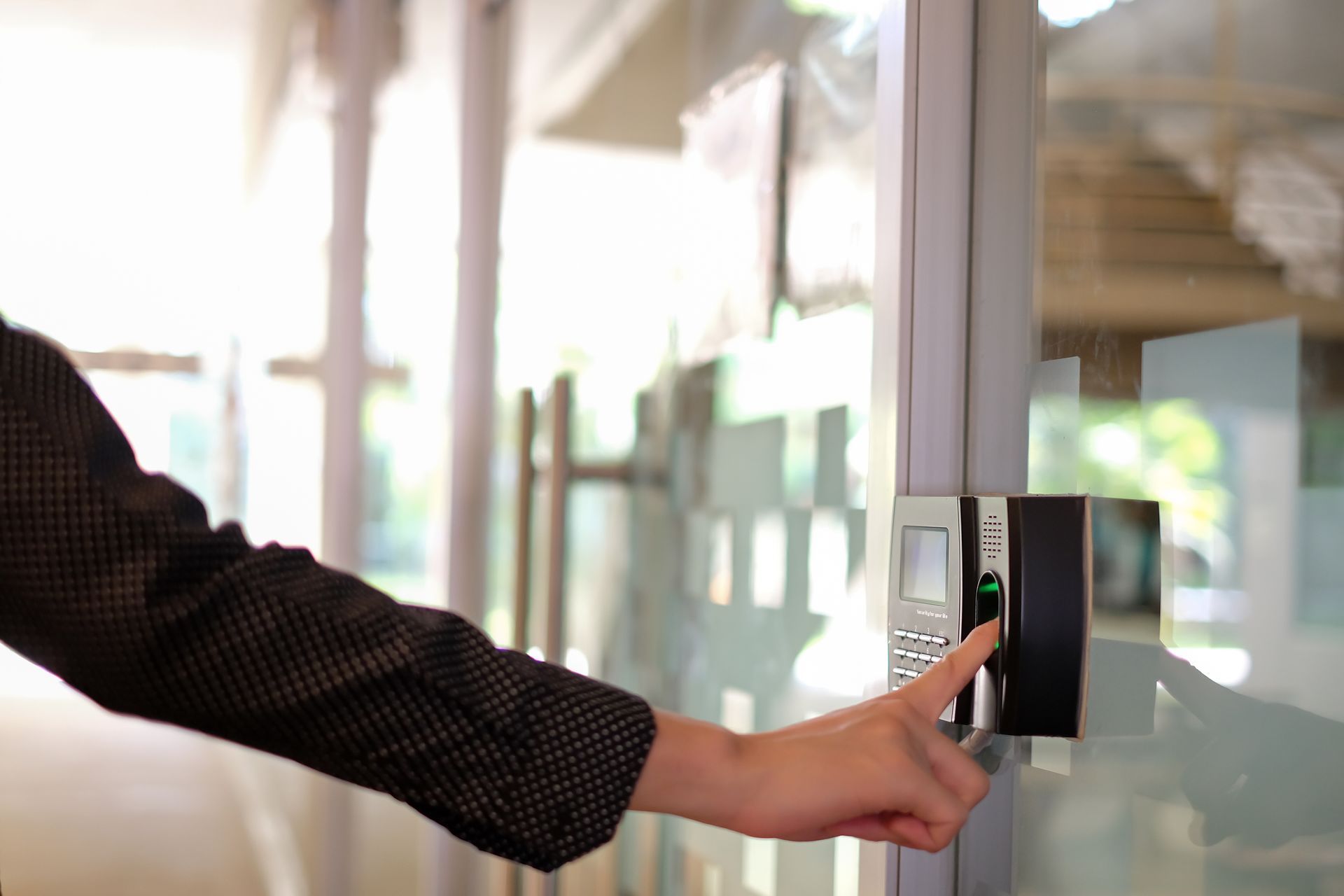 Person using a fingerprint biometric scanner to unlock a glass office door