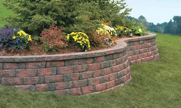 A brick wall with flowers in it and a tree in the middle.