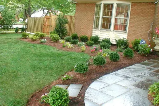 A brick house with a lush green lawn and a stone walkway leading to it.