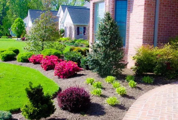 A brick house with a lush green lawn and bushes in front of it.