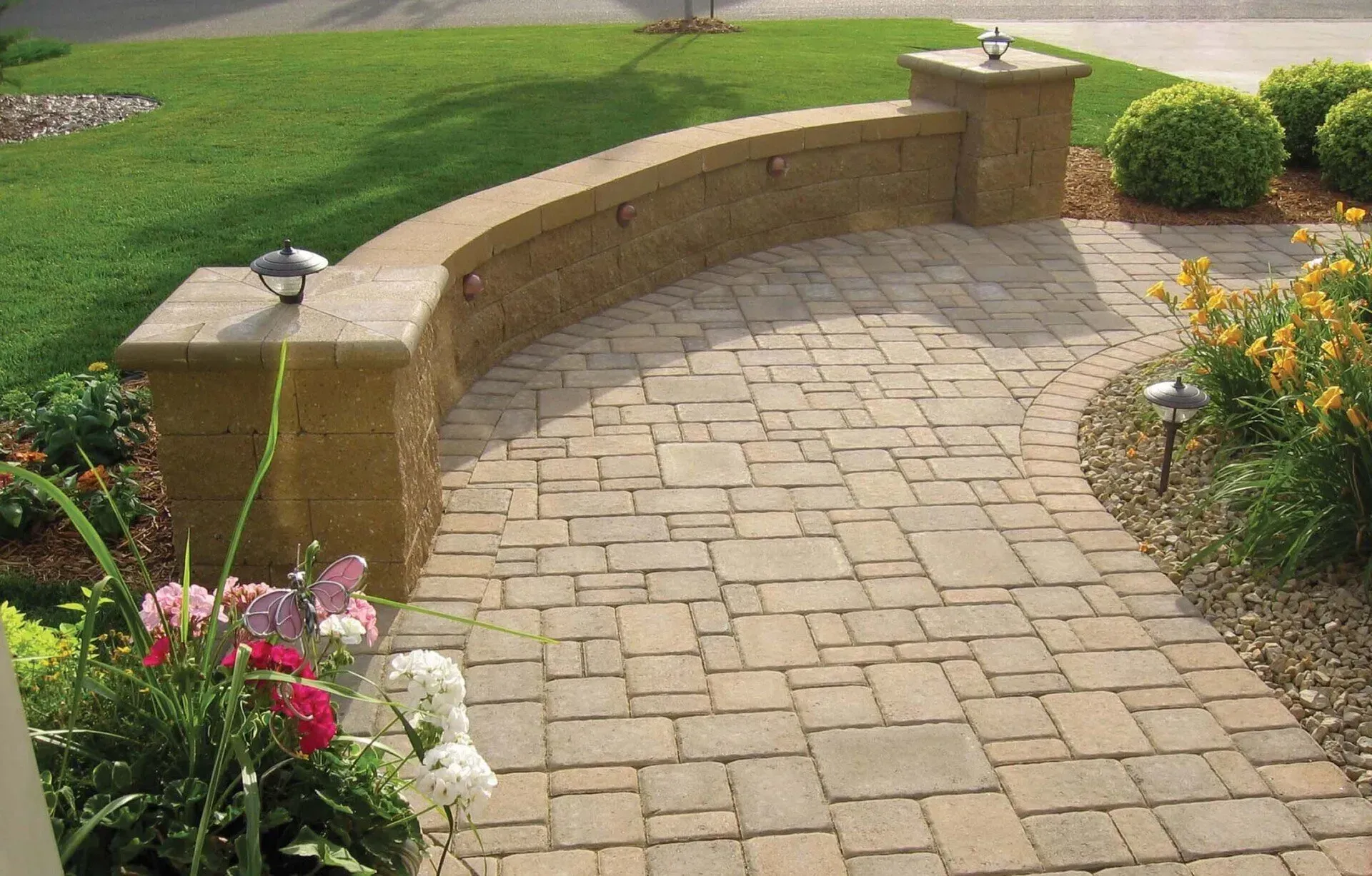 A brick walkway with a brick wall and flowers on the side