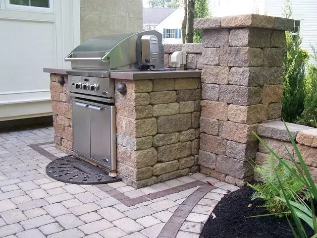 A grill is built into a stone wall on a patio