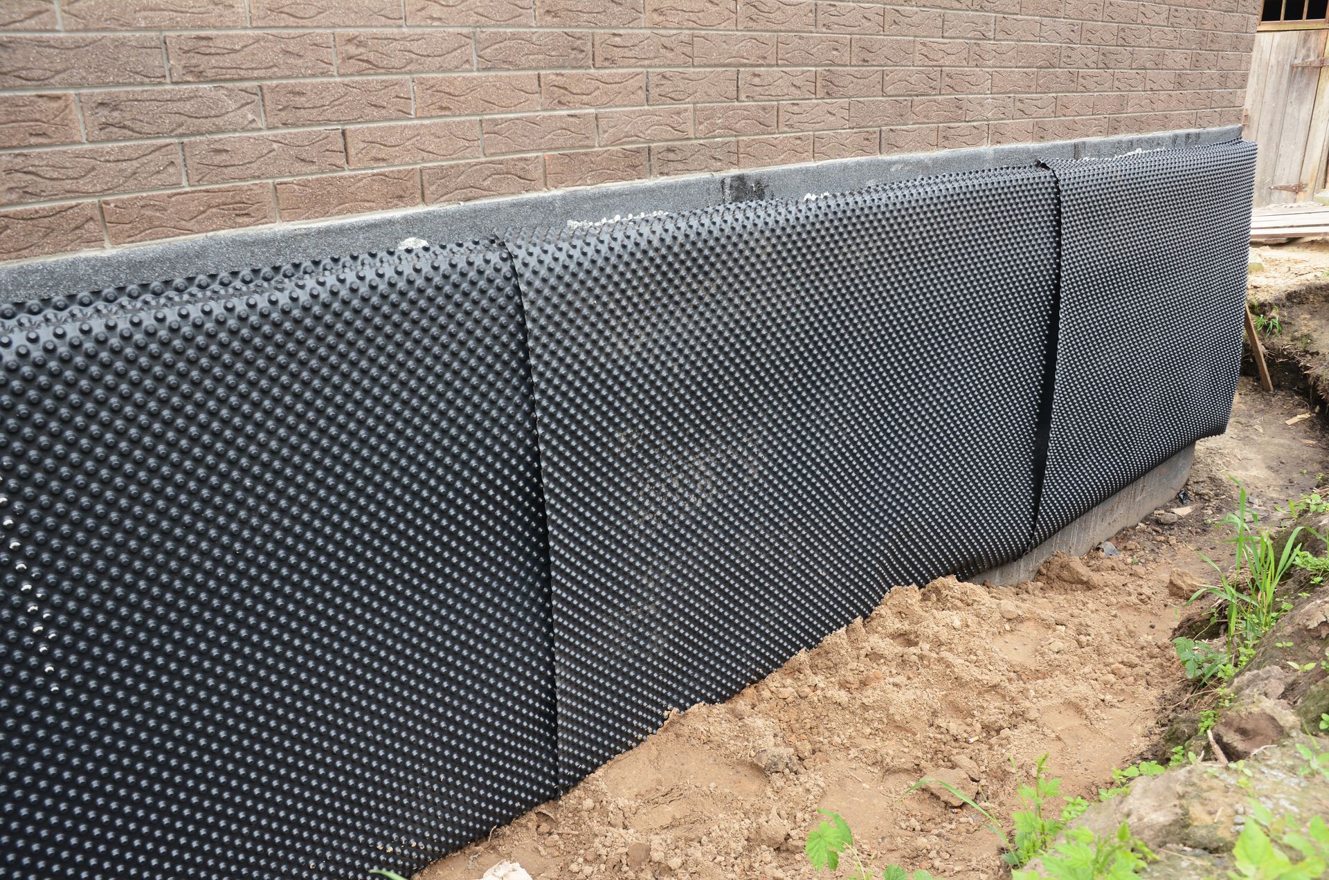 A brick wall with a black drainage mat on it.