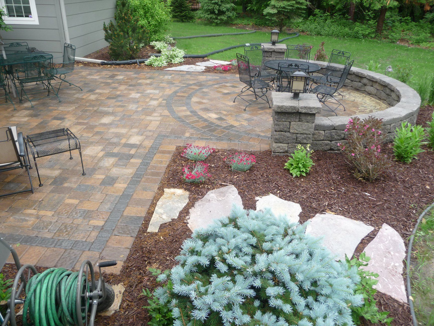 A patio with a table and chairs and a hose on the ground.