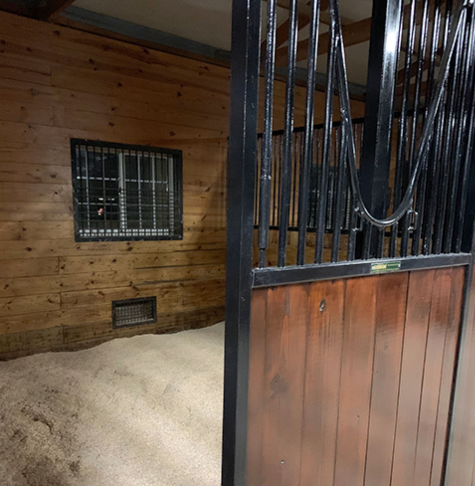 Indoor horse stable stall with wood walls, black metal bars, and straw bedding