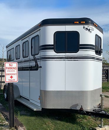 White RV trailer parked beside a no parking sign on grass, with tinted windows and black trim