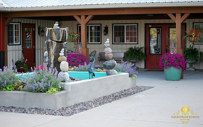 Courtyard garden with a stone fountain, flowers, and a covered walkway outside a building.