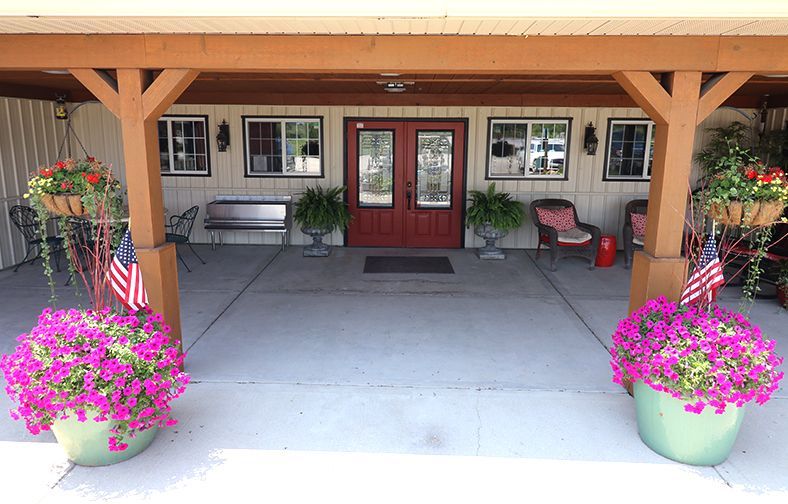 Front porch with red double doors, benches, and large pink flower pots under a wooden awning.