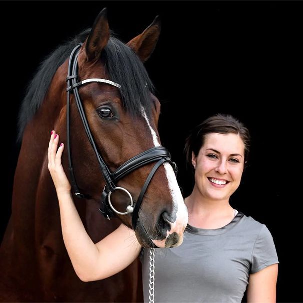 Smiling woman beside a brown horse with a white blaze, both against a black background