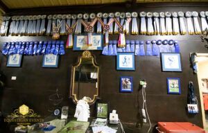 Wall of framed photos and hanging medals above a mantel with a mirror and small objects