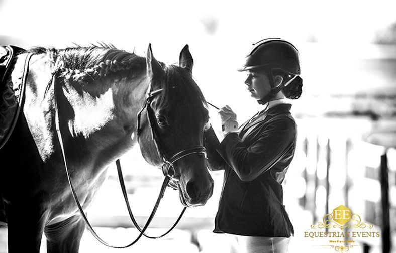 Person in helmet stands beside horse in black-and-white stable scene