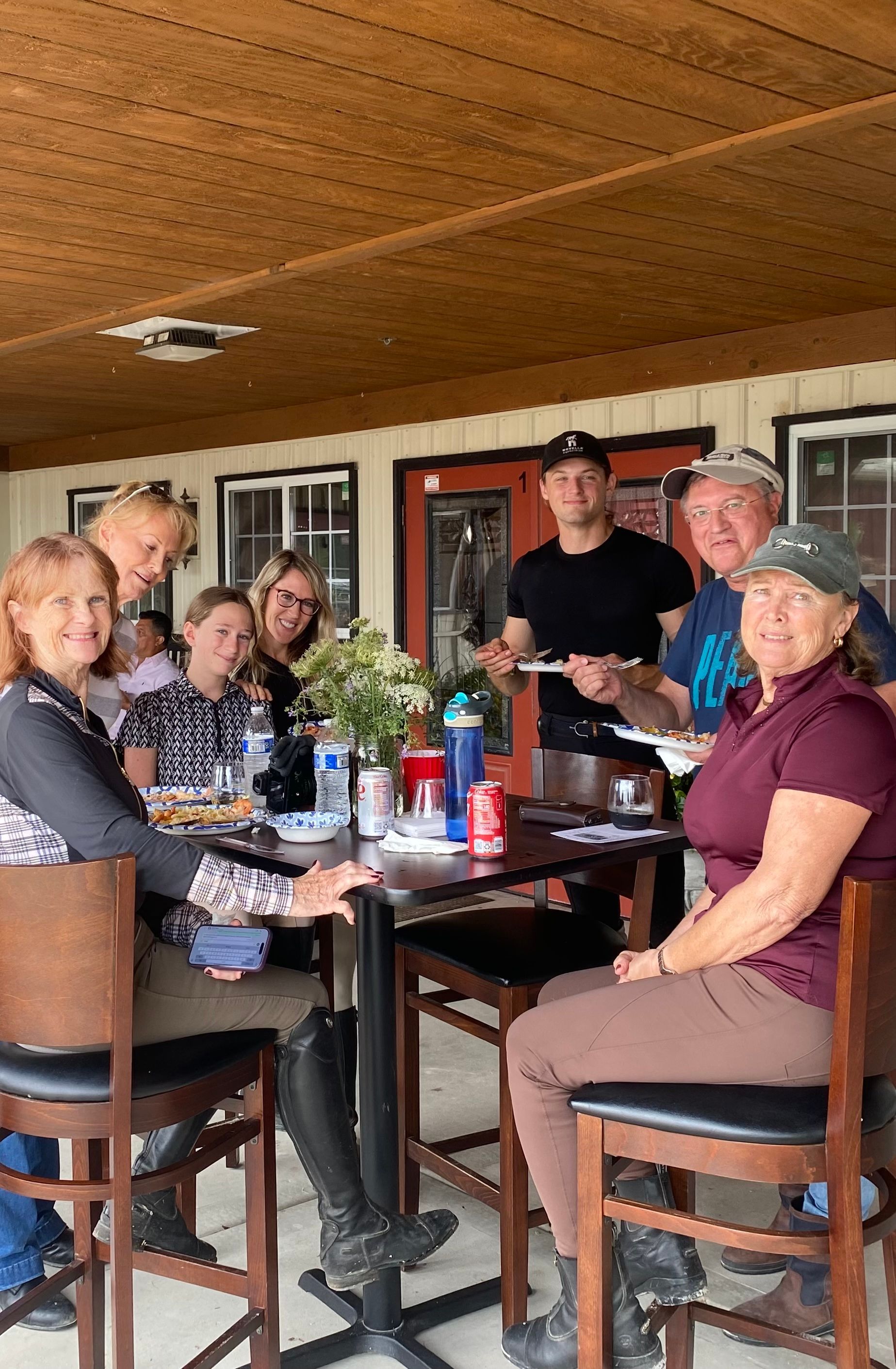 People sitting around a table on a covered porch, chatting and drinking together