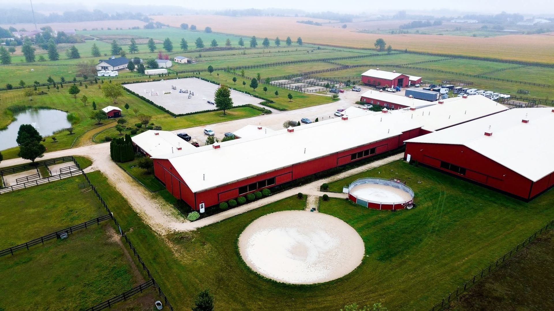 Aerial view of a red-and-white farm complex with silos, surrounded by green fields and roads.