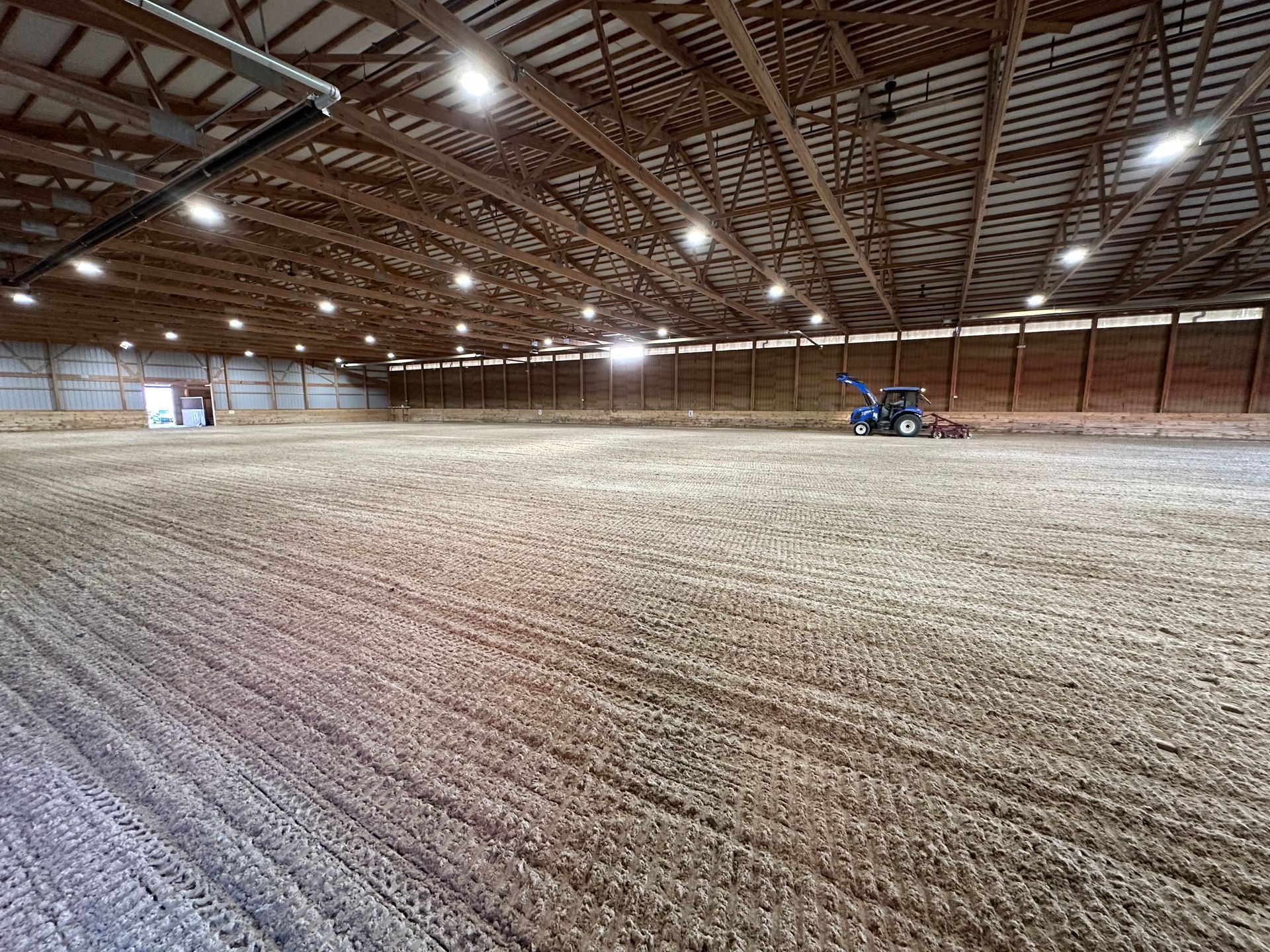 Large barn interior with exposed wooden rafters and a small tractor on a dirt-covered floor