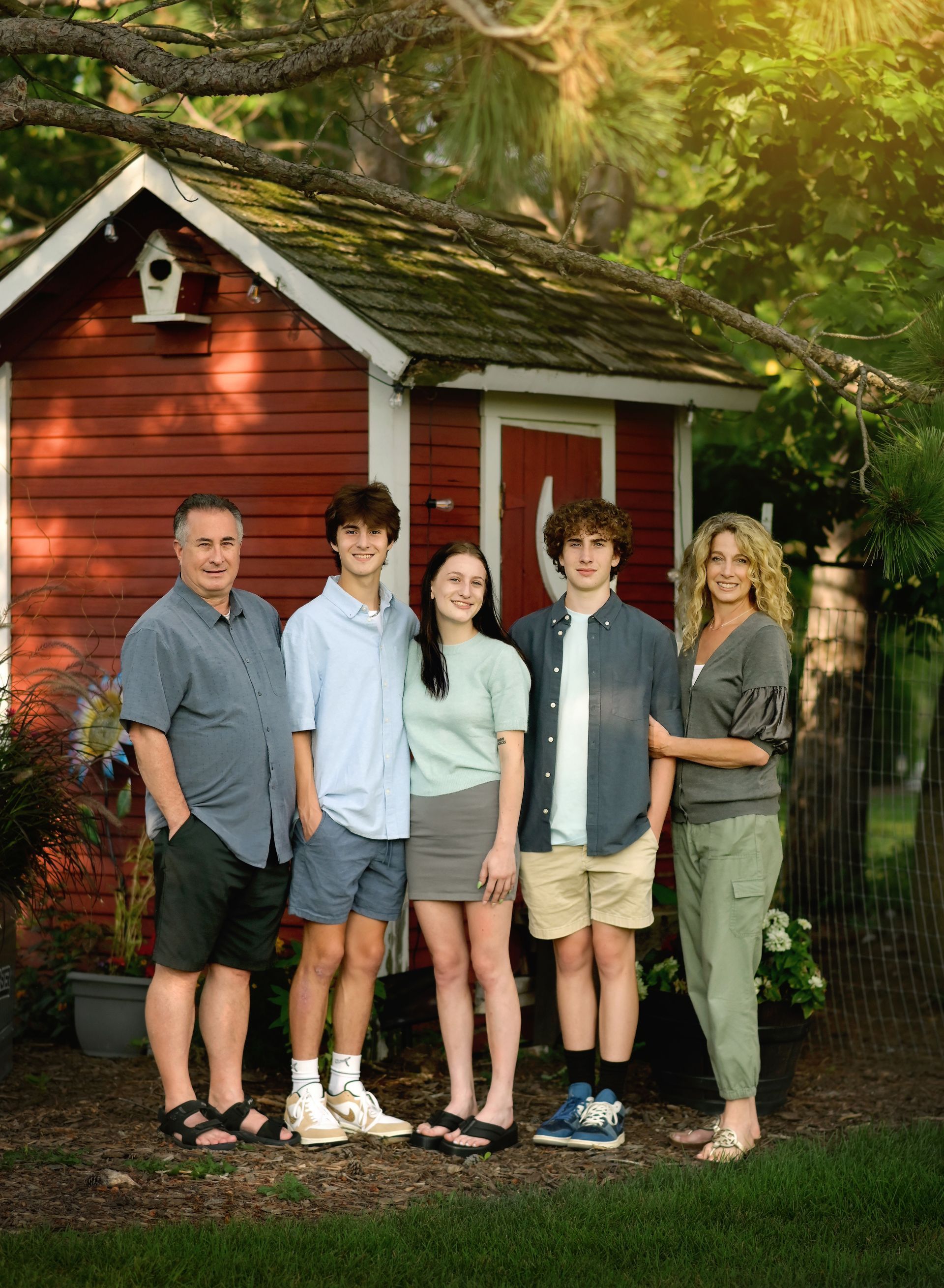 Five people standing in front of a red cabin in a wooded yard
