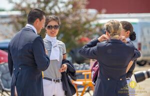 People in formal attire talking outdoors, with one woman adjusting her sunglasses.