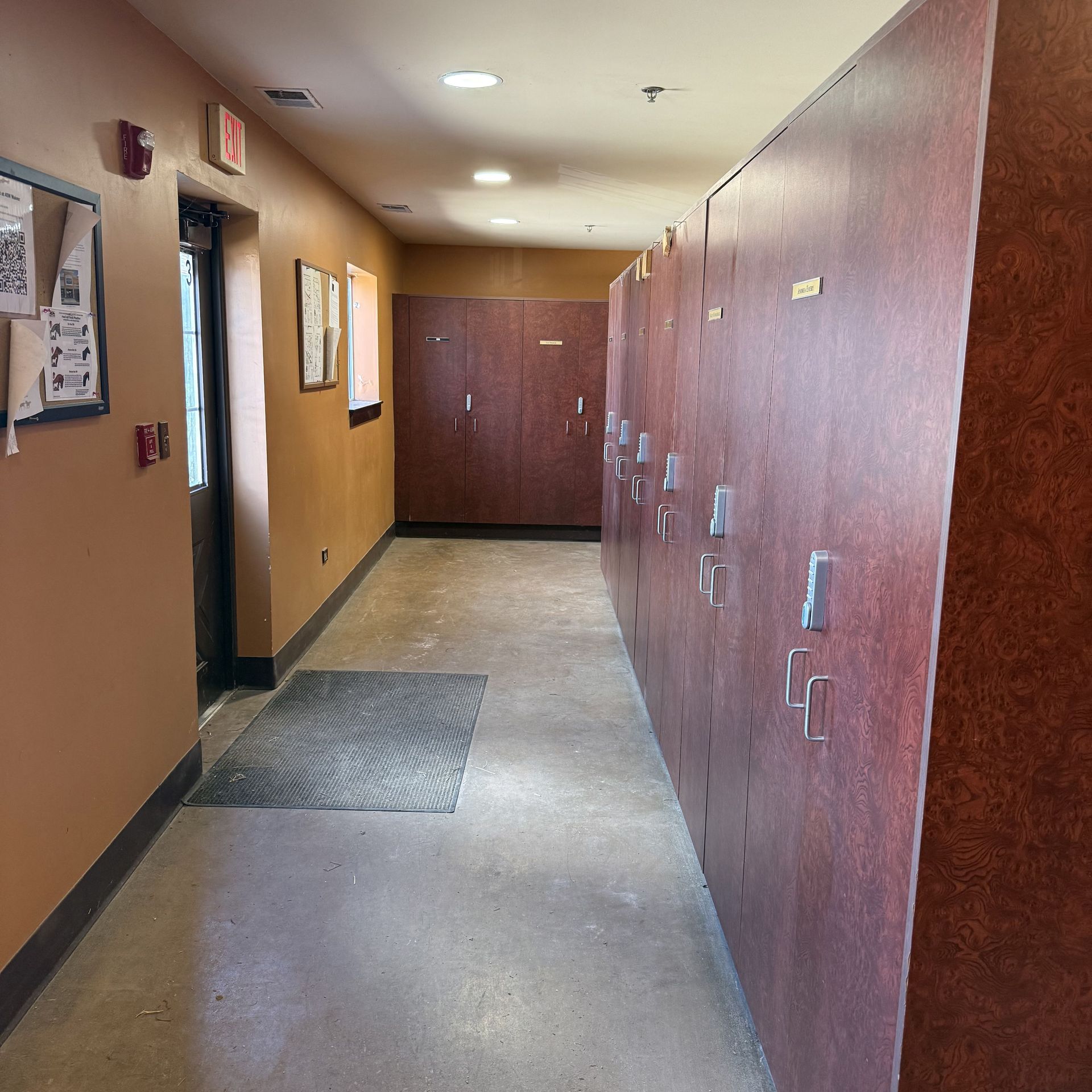 Narrow apartment hallway with tan walls, gray floor, and wood-paneled storage doors along one side.