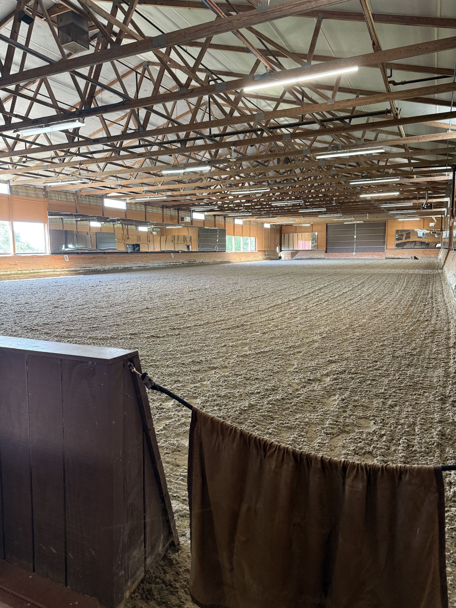 Indoor riding arena with a covered dirt floor and exposed wooden roof trusses