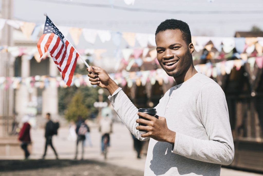 Person smiling and holding a small American flag outdoors at a festive street event