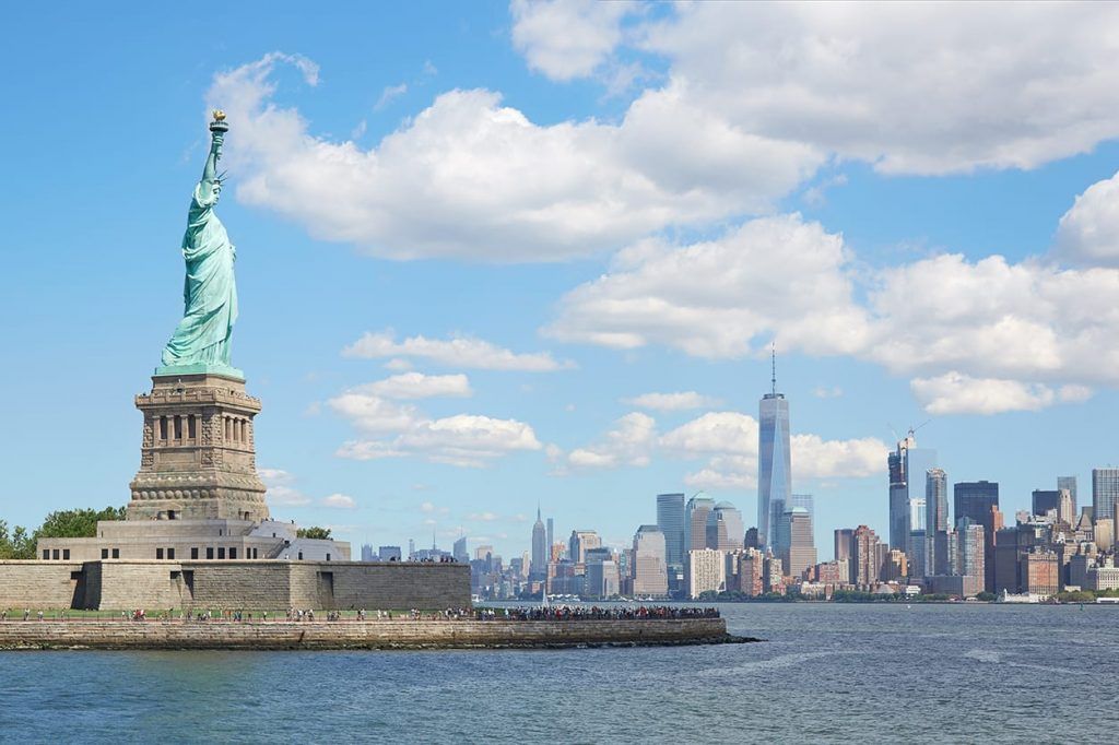 Statue of Liberty with Manhattan skyline across the water under a partly cloudy sky