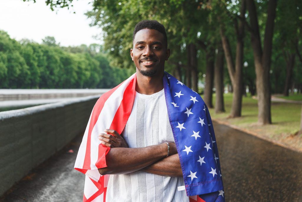 Man smiling on a riverside path, wrapped in an American flag