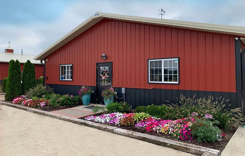 Red building with black trim and flower beds along a gravel driveway