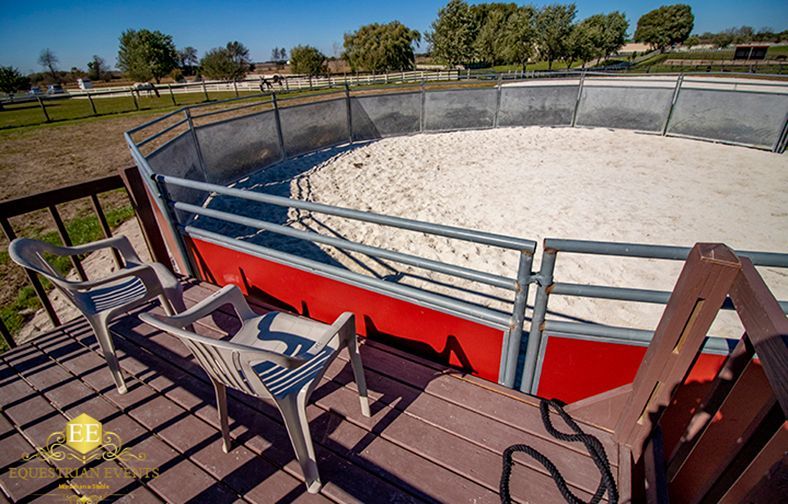 Empty fenced rodeo arena with red and gray railings and chairs on a wooden deck