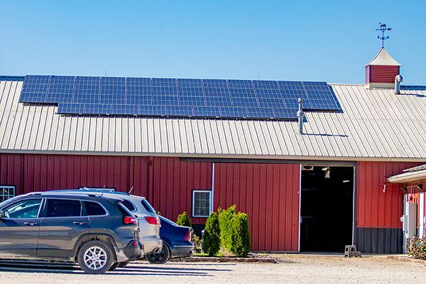 Red barn with solar panels and parked SUV under a clear blue sky