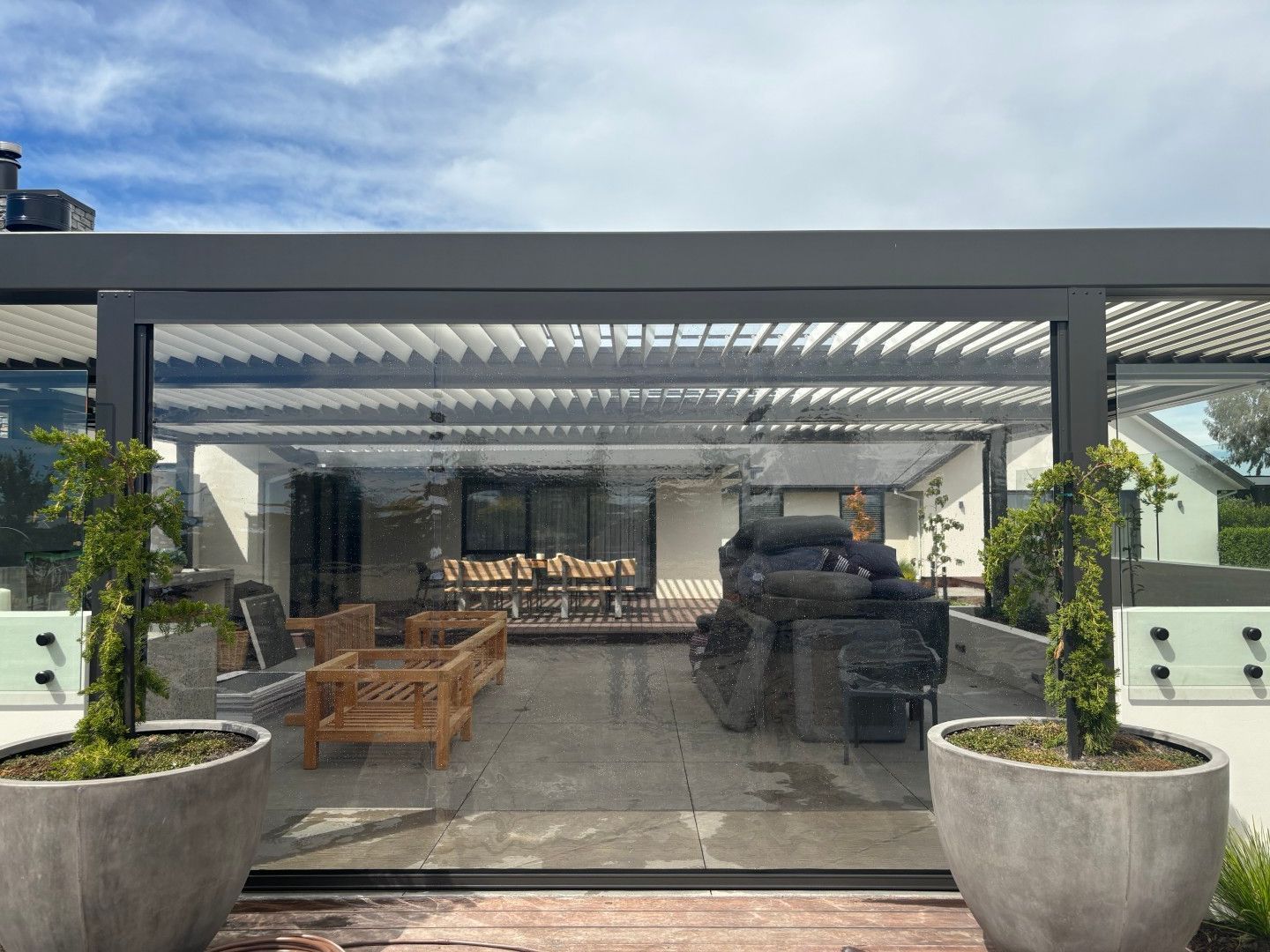 A patio with a pergola and potted plants in front of a house.
