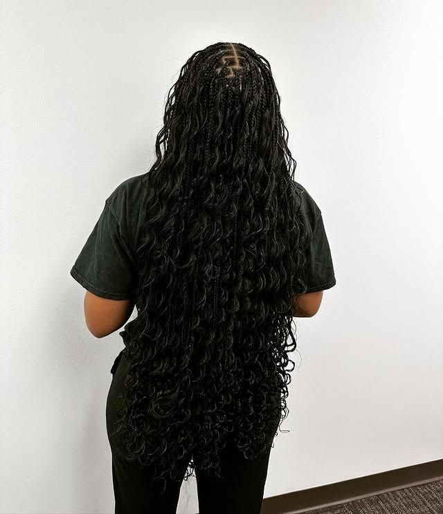 Person standing with back to camera, wearing a black shirt and black pants, with very long wavy dark hair.