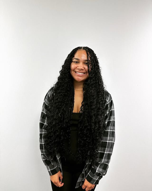 Person smiling against a plain white wall, wearing a black top and gray plaid shirt.