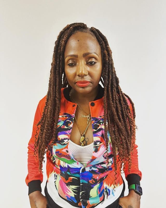 Woman wearing a colorful jacket and braids, looking down against a plain white background.