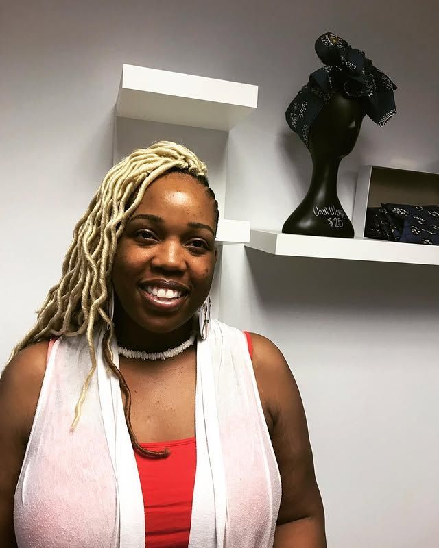 Smiling woman in a red top and white vest standing in an office with shelves and decor behind her