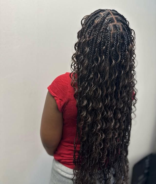 Person seen from behind with long curly black hair, wearing a red top and light gray pants.